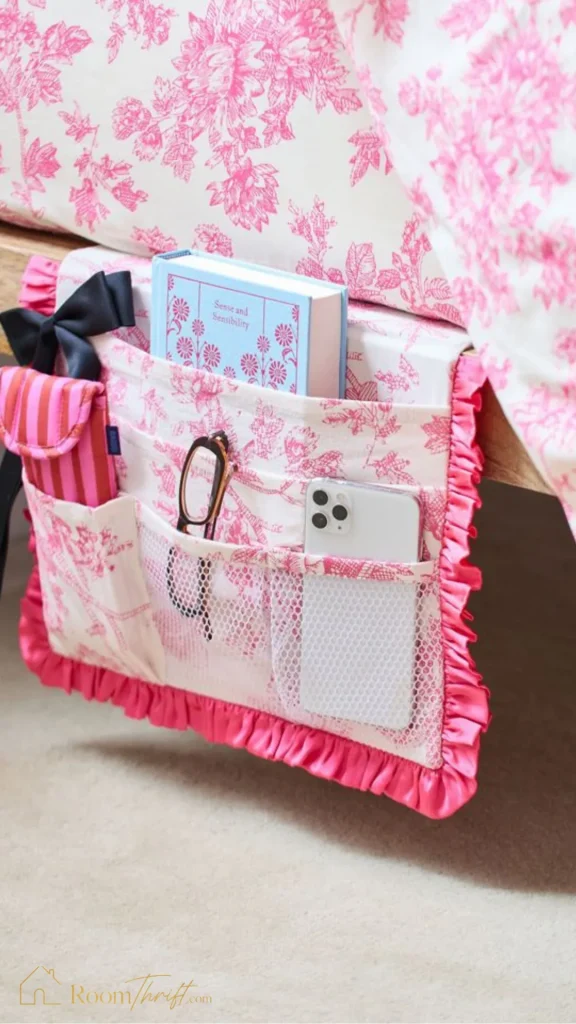 Clever small bedroom ideas featuring a pink floral fabric bedside caddy tucked into a mattress frame to hold essentials.