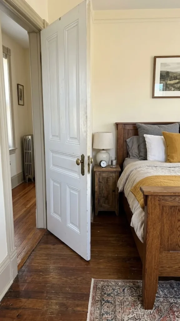 An open white bedroom door showing tight clearance next to a wooden nightstand and bed frame, highlighting important layout factors when planning the right room size for king bed.