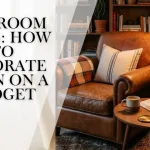 A blog post header banner graphic showing cozy den room decorating ideas with text overlay that reads "DEN ROOM IDEAS: HOW TO DECORATE A DEN ON A BUDGET" across a moody reading space with a classic brown leather armchair, dark navy walls, and a wooden side table.